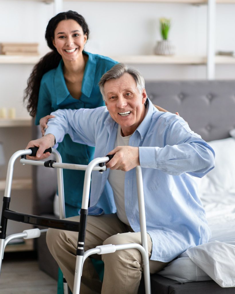 female-nurse-helping-elderly-male-with-walking-frame-stand-up-from-bed-at-home-professional-care.jpg