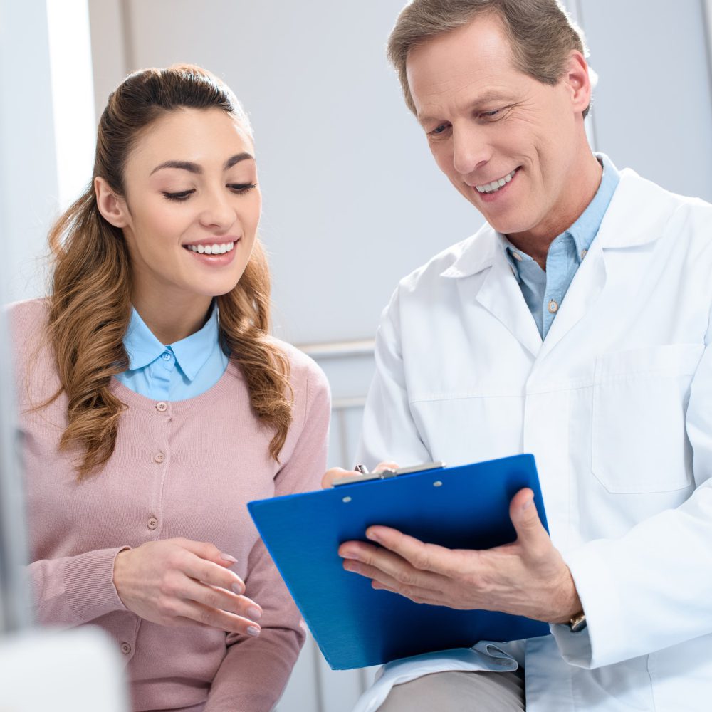 handsome-doctor-showing-something-in-clipboard-to-smiling-patient-in-clinic.jpg